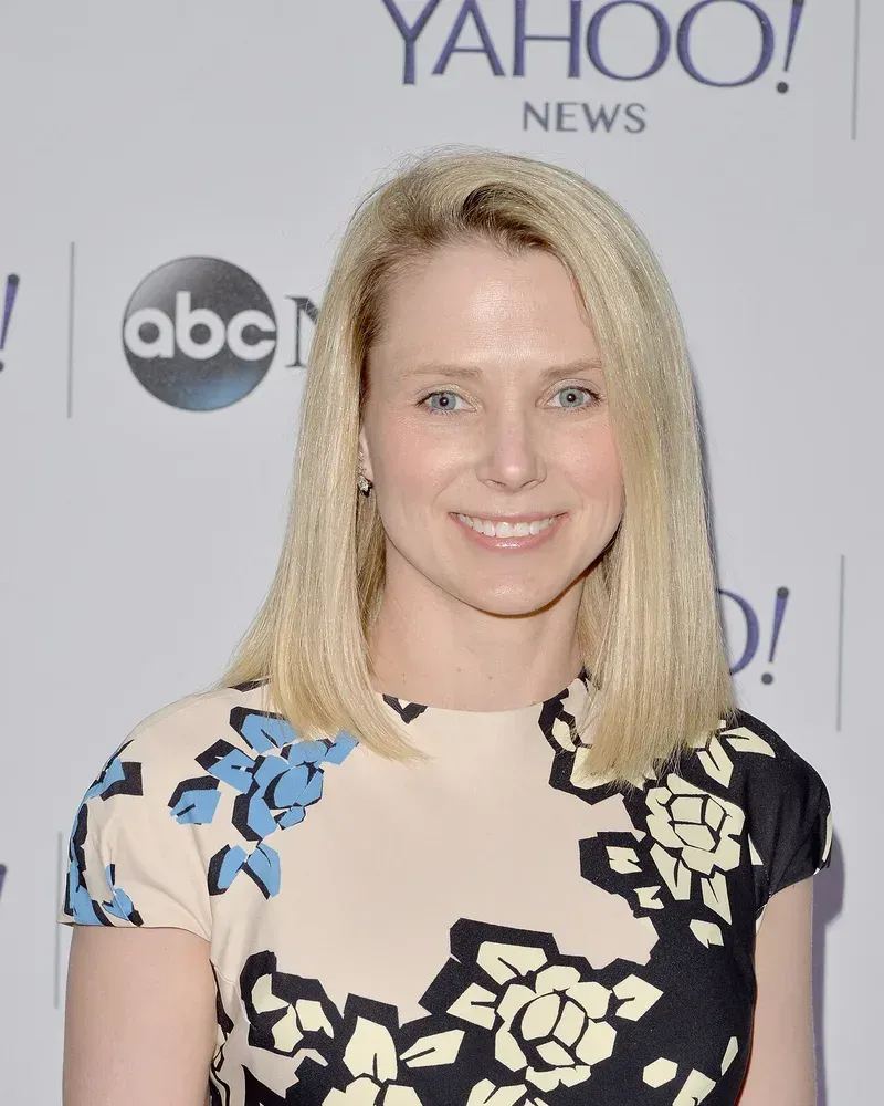 ماريسا ماير تبتسم بفستان مزين بالزهور أمام لوحة عليها شعار Yahoo News