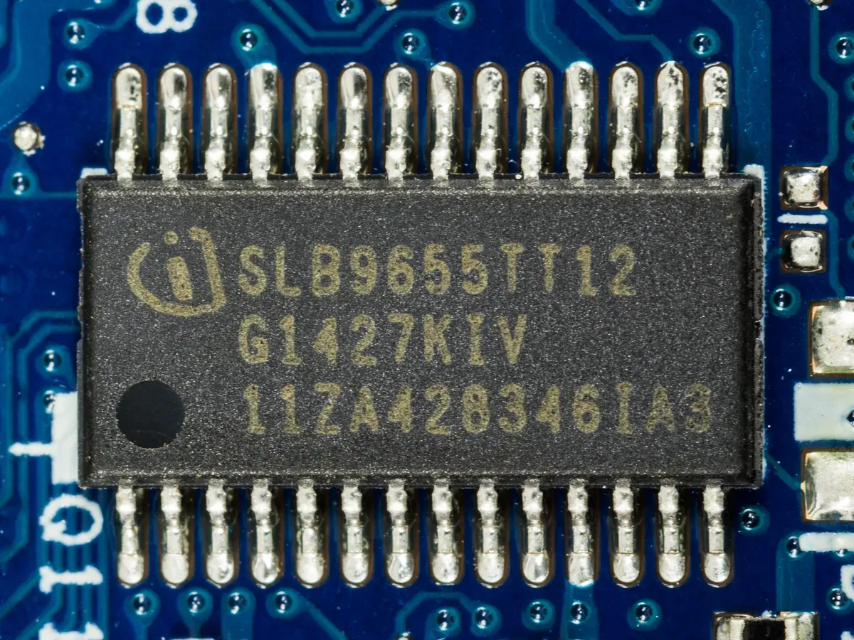 صورة مقربة لشريحة TPM من إنتاج Infineon ملحومة على اللوحة الأم لجهاز محمول، وحولها مسارات ومكونات اللوحة