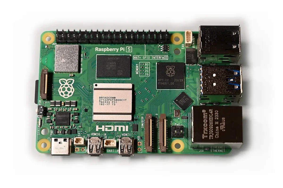 لوحة Raspberry Pi 5 خضراء من الأعلى، عليها شريحة المعالج Broadcom الفضية في الوسط وشريحة الذاكرة فوقها وشريحة RP1 بجانبها، ومنافذ USB وEthernet على اليمين ومنفذا HDMI الصغيران ومنفذ USB-C للطاقة في الأسفل، وصف دبابيس GPIO في الأعلى