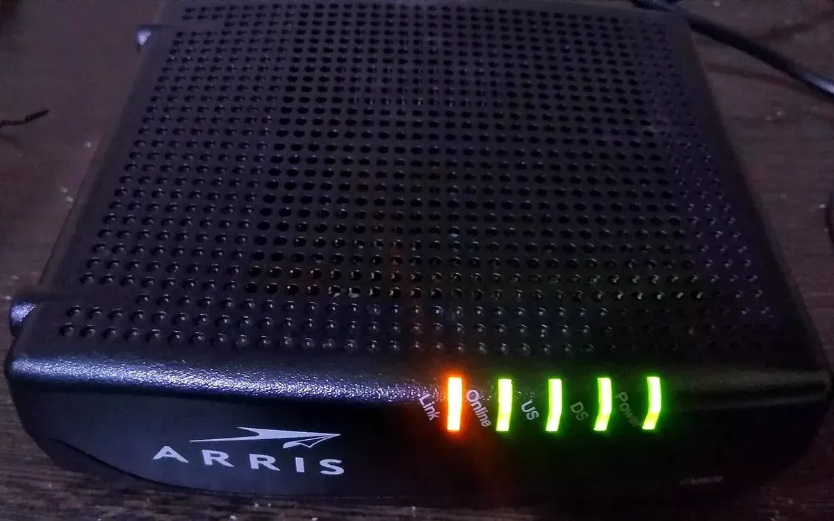 مودم كابل أسود من ARRIS بأضواء خضراء وصفراء في الواجهة تشير إلى حالة التنزيل والرفع والاتصال