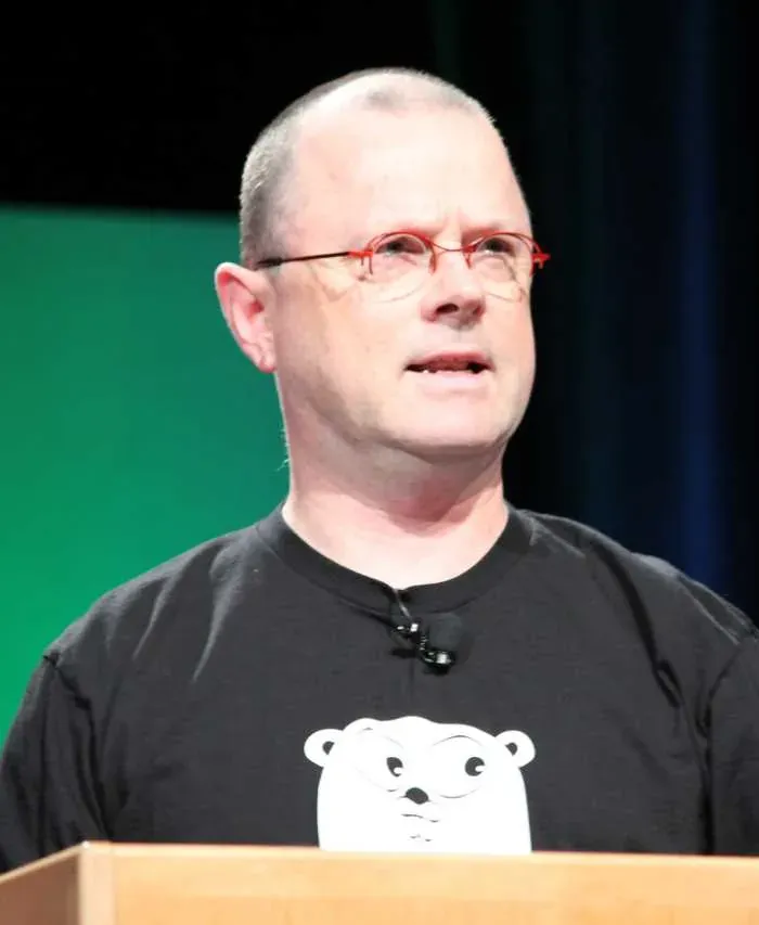 صورة روب بايك بنظارة حمراء وقميص أسود عليه دب أبيض يتحدث من منصة في مؤتمر OSCON
