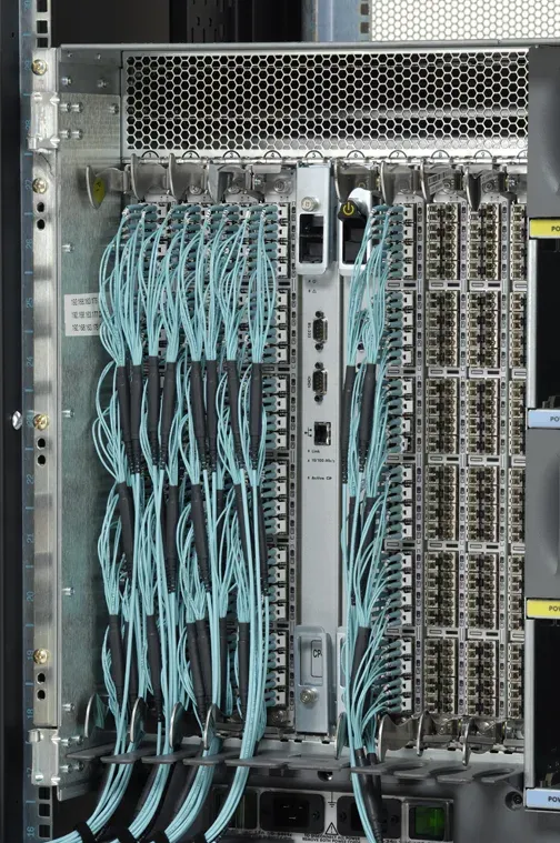 محول Fibre Channel كبير من فئة Director مثبت في خزانة، فيه بطاقات منافذ عمودية كثيرة ومئات من كابلات الألياف الضوئية بلون أزرق فاتح متصلة بالمنافذ ومرتبة في حزم