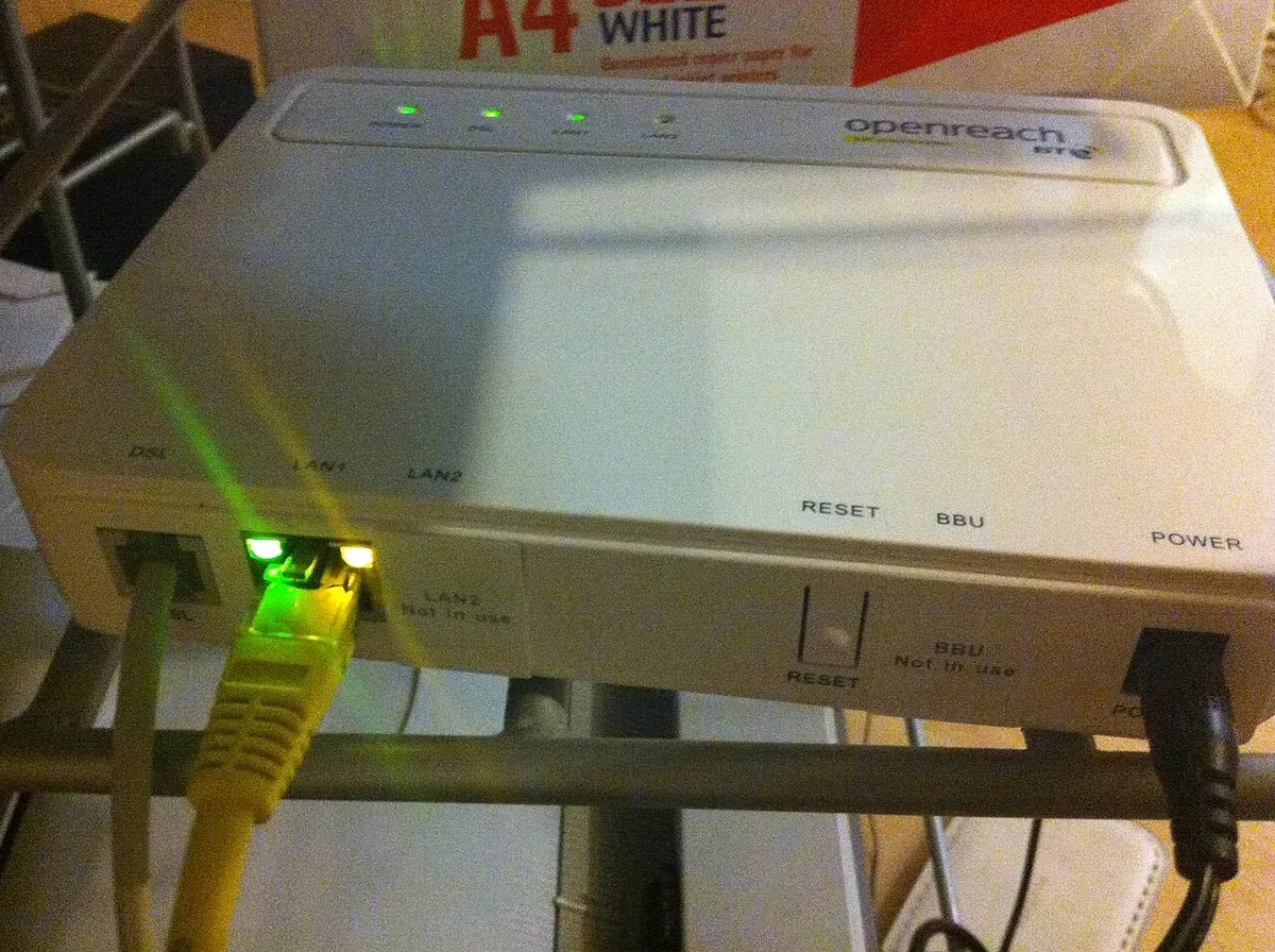 مودم VDSL أبيض صغير من Openreach على رف، فيه منفذ LAN واحد يخرج منه كابل Ethernet أصفر، وزر Reset ومنفذ للكهرباء