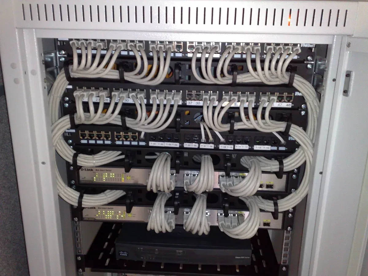 خزانة شبكة بمقاس 19 بوصة فيها صفوف من لوحات التوصيل Patch Panels، وتحتها Switches مدارة من D-Link، وبينها كابلات قصيرة رمادية مرتبة في حلقات