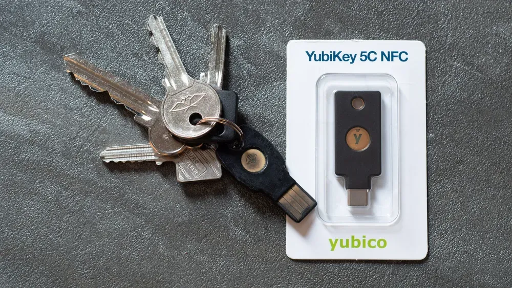 مفتاح YubiKey أسود بمنفذ USB-A معلق في سلسلة مفاتيح بجانب مفاتيح أبواب، وبجانبه مفتاح YubiKey 5C NFC جديد بمنفذ USB-C في غلافه البلاستيكي