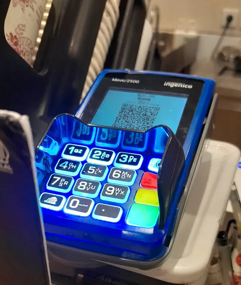 جهاز دفع محمول بلوحة أرقام مضاءة باللون الأزرق، وعلى شاشته الصغيرة رمز QR يعرضه للعميل